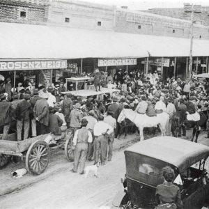 Mixed crowd with cars and horses on crowded town street