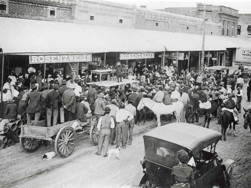 Mixed crowd with cars and horses on crowded town street