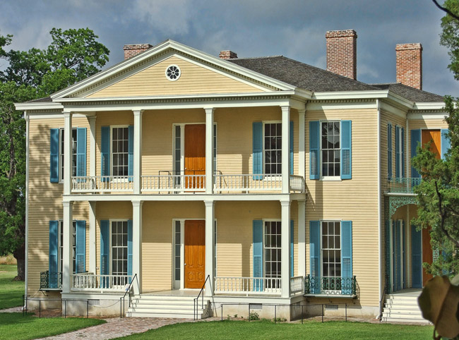 yellow two-story house with covered porch and balcony and light blue stutters