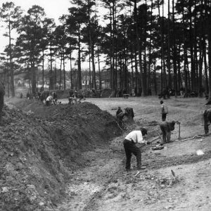 Group of African-American men digging in field with mounds of dirt behind them