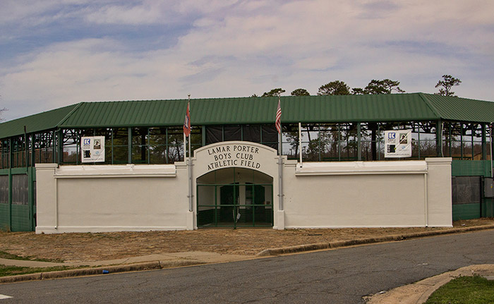 Entrance gate to athletic field with green metal roof and paved road in foreground