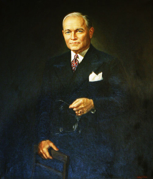 Older white man in suit holding a pair of glasses
