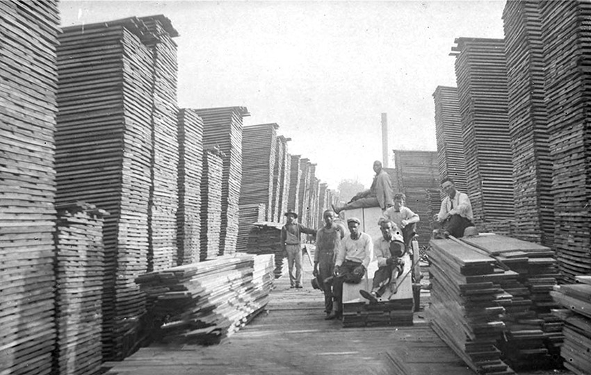 Group of men standing amid stacks of lumber