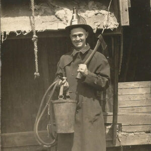 White man in uniform with firemen's hat bucket and hatchet on set