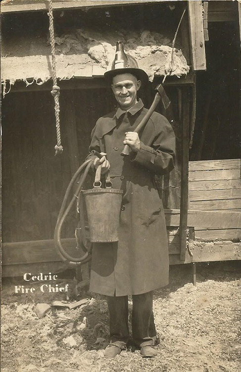 White man in uniform with firemen's hat bucket and hatchet on set