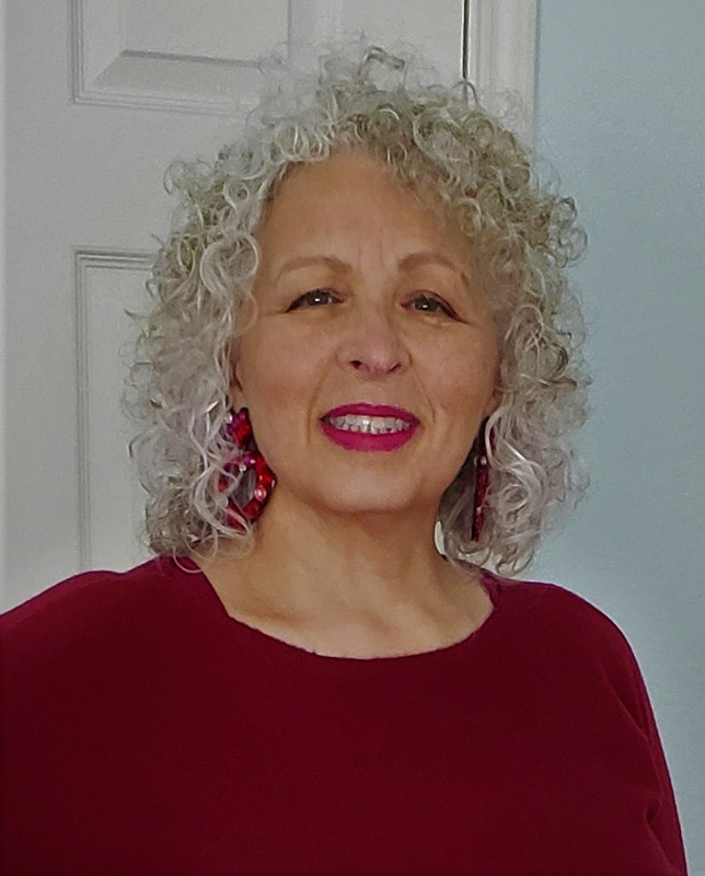 African American woman with long curly gray hair smiling in red shirt and earrings
