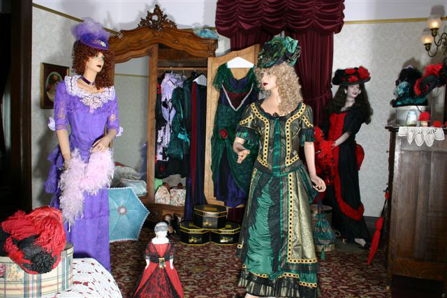 Two mannequins wearing fancy dresses in room with fashion artifacts