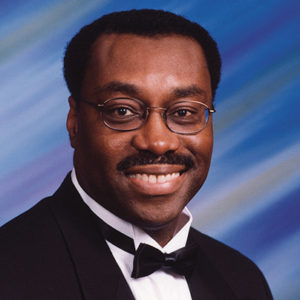 African-American man with glasses and mustache smiling in tuxedo