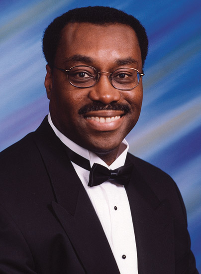 African-American man with glasses and mustache smiling in tuxedo