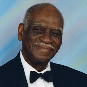 Older African-American man with mustache smiling in suit and tie