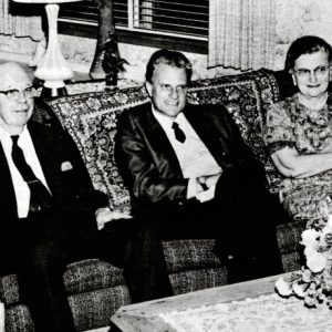 Older white men in suits sitting on a couch with white woman