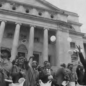 White men and women throwing "pennies" outside multistory building with four front columns and large dome