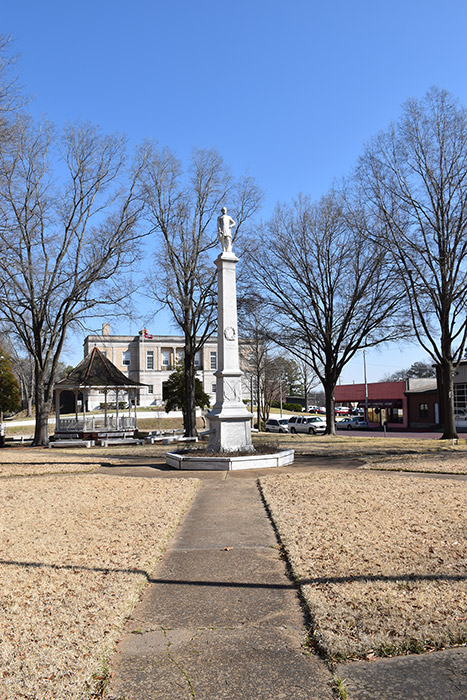 Tall stone monument and gazebo on park with town buildings in the background