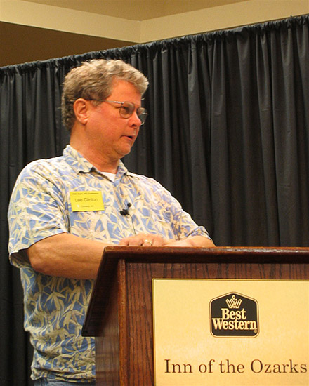 White man with glasses in Hawaiian shirt speaking at lectern