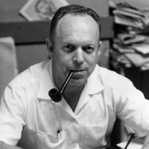 White man in white short-sleeved shirt smoking a pipe and holding a pen