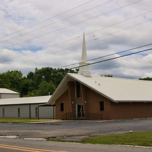 Brick church building with steeple and brick sign on parking lot