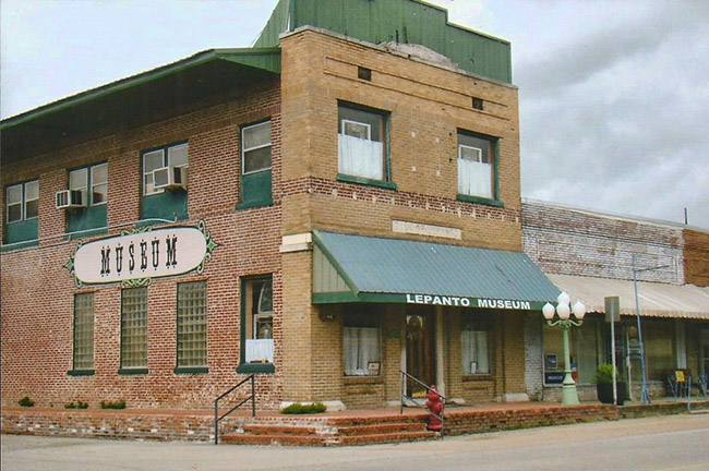 Two-story brick storefront with "Museum" written on the side with green roof and awning over front entrance