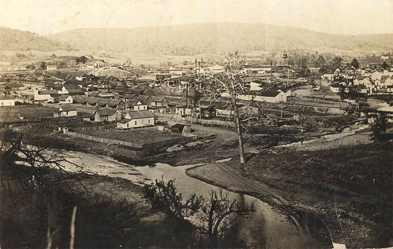 View overlooking river and single-story buildings with town and hills in the background