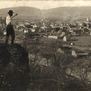 Man in hat standing on rock outcropping pointing towards town