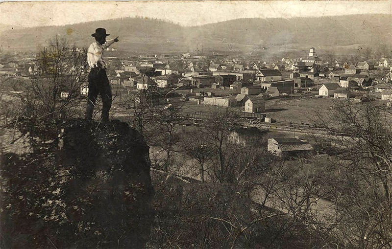 Man in hat standing on rock outcropping pointing towards town