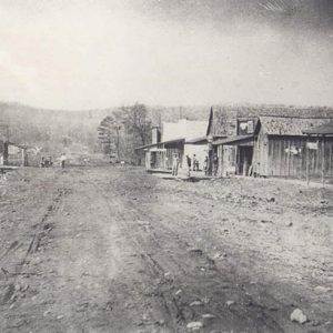 Dirt road with single-story storefronts and car in the background