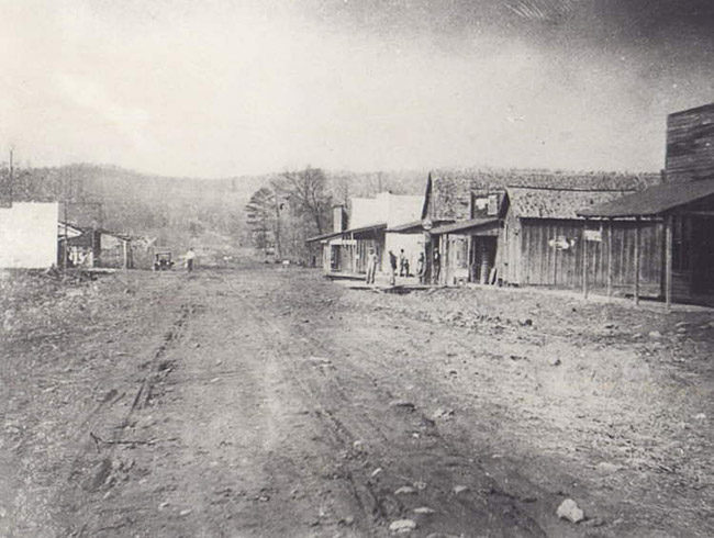 Dirt road with single-story storefronts and car in the background