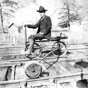 White man in hat and striped suit sitting on railroad bike