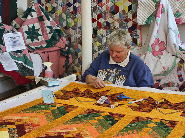 White woman in sweatshirt working on a colorful quilt