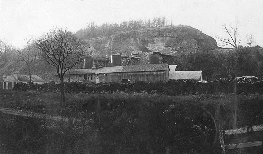 Single-story storefront and lime kiln building alongside hill with trees in the foreground