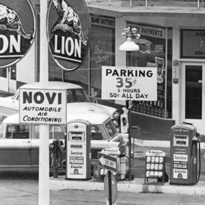 Two cars at service station with Lion advertisements on pole in the foreground