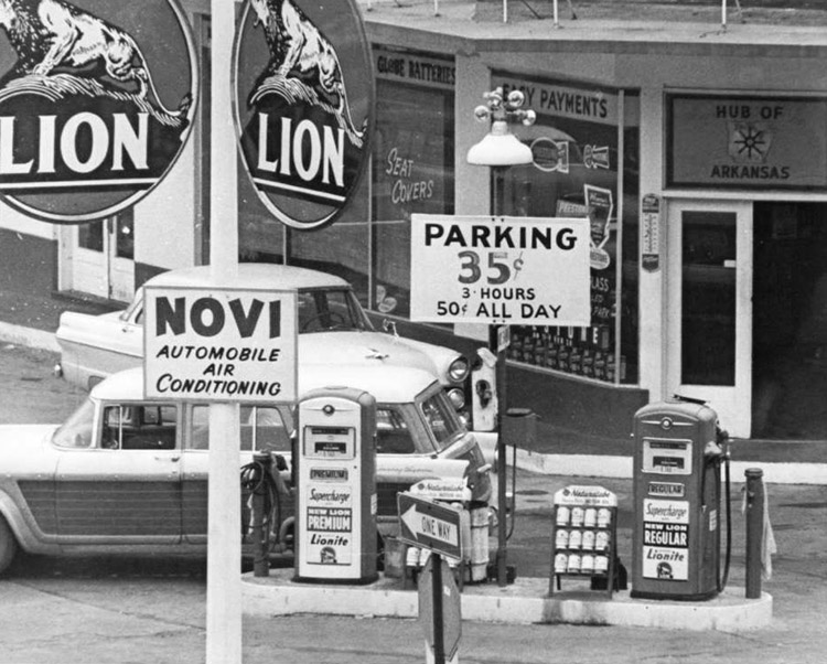 Two cars at service station with Lion advertisements on pole in the foreground