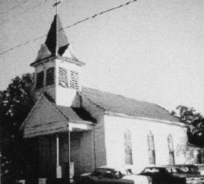 Church building with central bell tower and cars parked alongside