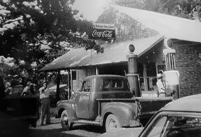 White men and trucks outside single-story storefront with covered porch and Coca-Cola sign