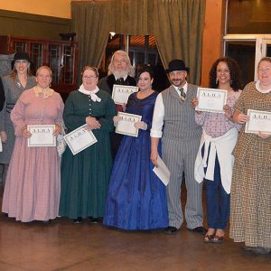 Group of white men and women in period costume holding certificates