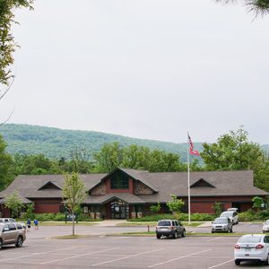 Single story brick building with parking lot and tree covered hills in the background