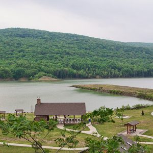 Lake with pavilions and walking paths with tree covered hill in the background