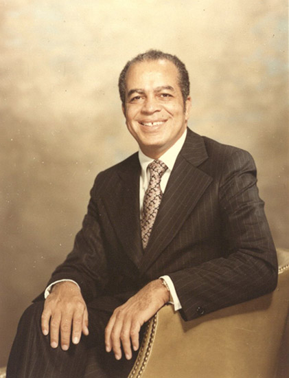 African-American man smiling in striped suit and tie sitting in leather chair