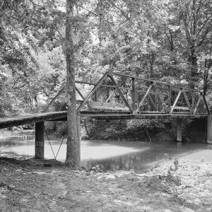 Steel truss bridge with wooden platform over river