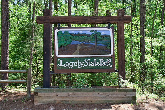 Hanging "Logoly State Park" sign with flower bed in forested area