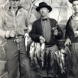 Three white men in hats with fishing poles and fish on a line