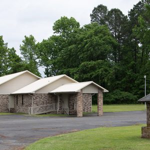 Single-story brick church building with box gable roofs and covered entrance on parking lot