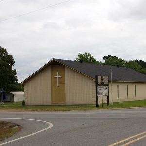 Single-story brick church building with cross and box gable roof on street corner