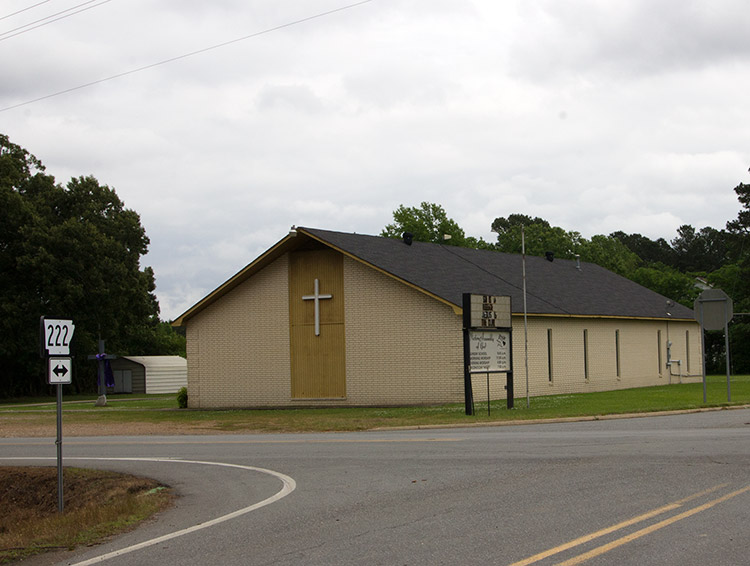 Single-story brick church building with cross and box gable roof on street corner