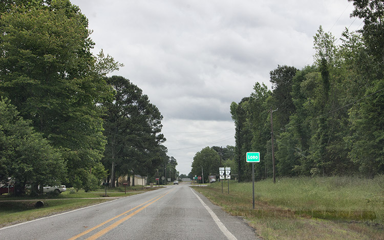 Two-lane rural road with Lono sign and other road signs on its right side