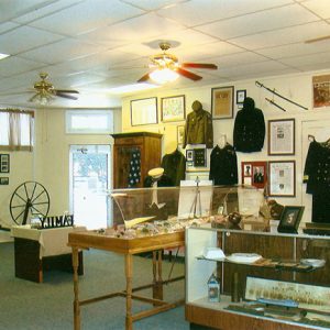 Interior of museum with military artifacts on display in glass cases and uniforms on wall with framed documents