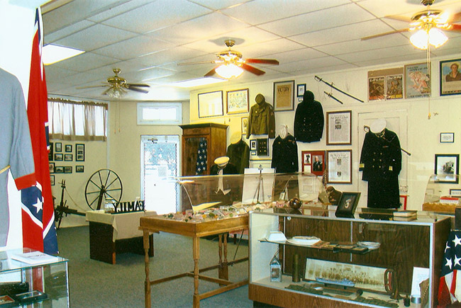 Interior of museum with military artifacts on display in glass cases and uniforms on wall with framed documents