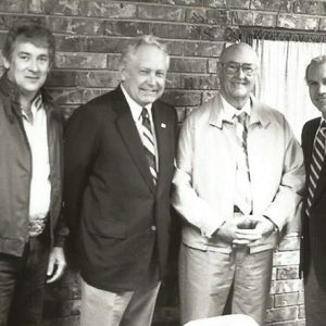 Four white men standing and smiling with brick wall behind them