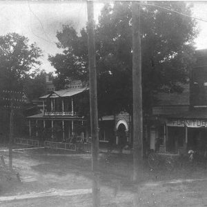 Horse drawn wagon on dirt road outside multistory storefront buildings with power lines in the foreground