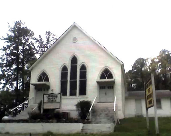 symmetrical white church building with two entrances with stairs leading up to them and sign