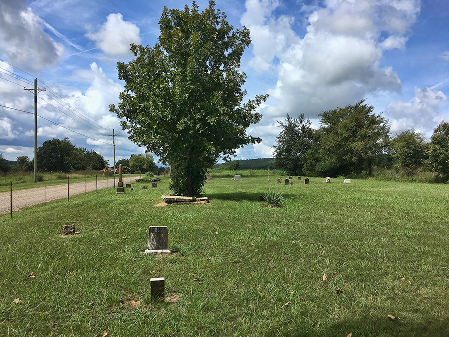 Monuments and gravestones with tree in cemetery on dirt road